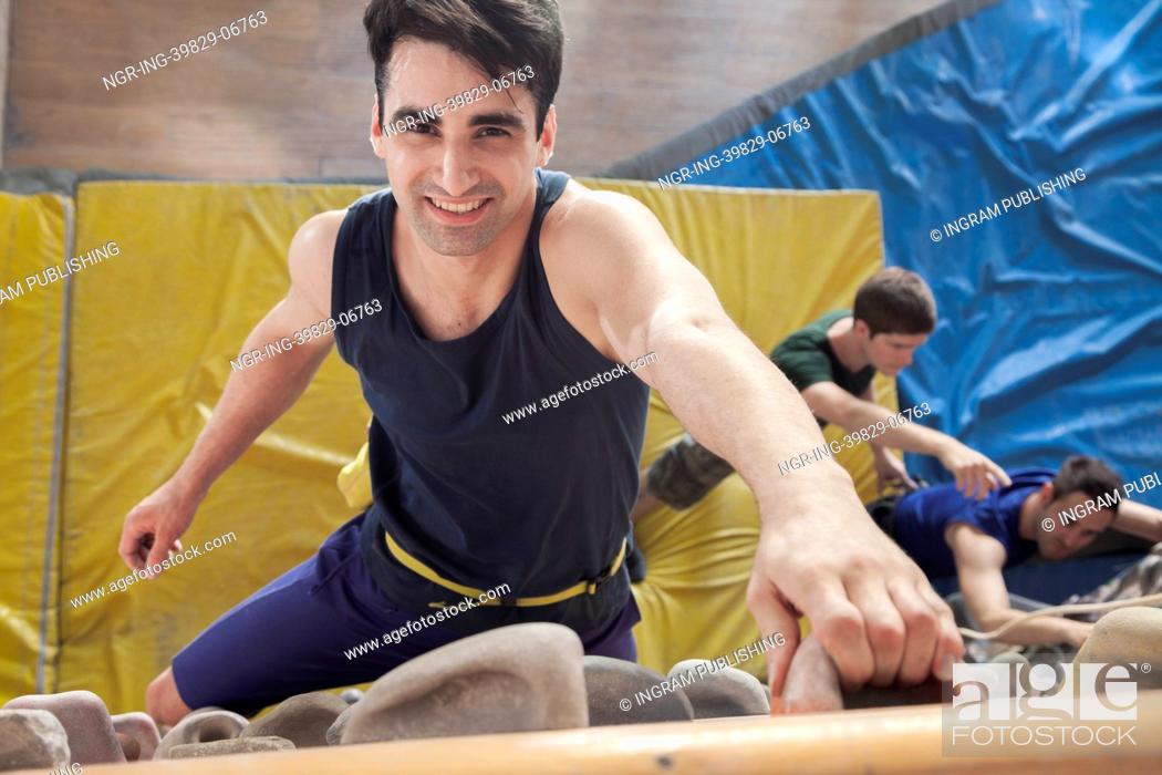 Stock Photo: Smiling young man climbing up a climbing wall in an indoor climbing gym, directly above.