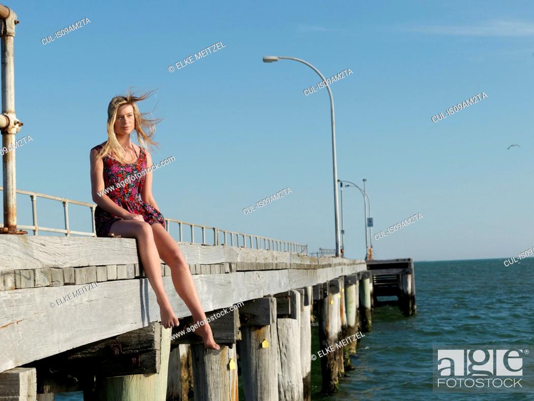 Stock Photo: Young woman sitting on breezy pier, Altona, Melbourne, Victoria, Australia.