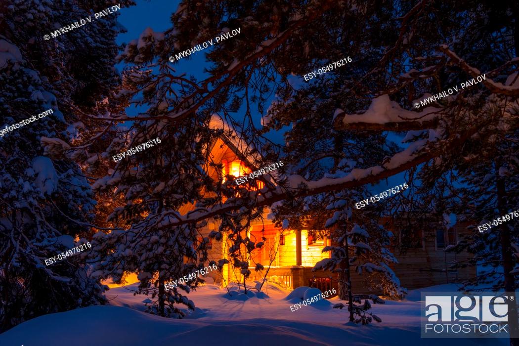 Stock Photo: Evening winter forest. Pine branches covered with large caps of snow. Lighted cottage in the background.