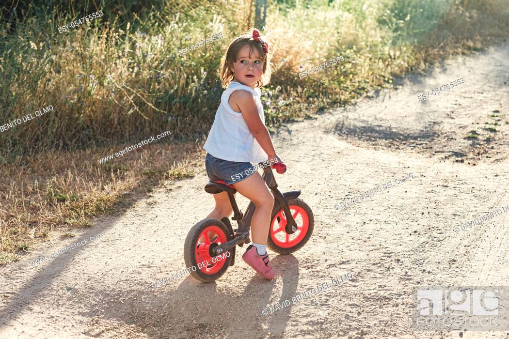 Stock Photo: Blond hair girl riding a bicycle on a dirt road.
