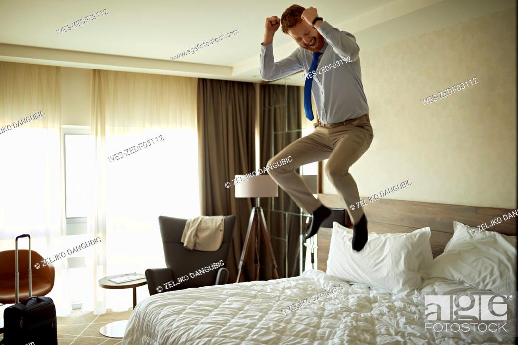 Stock Photo: Excited businessman jumping on bed in hotel room.