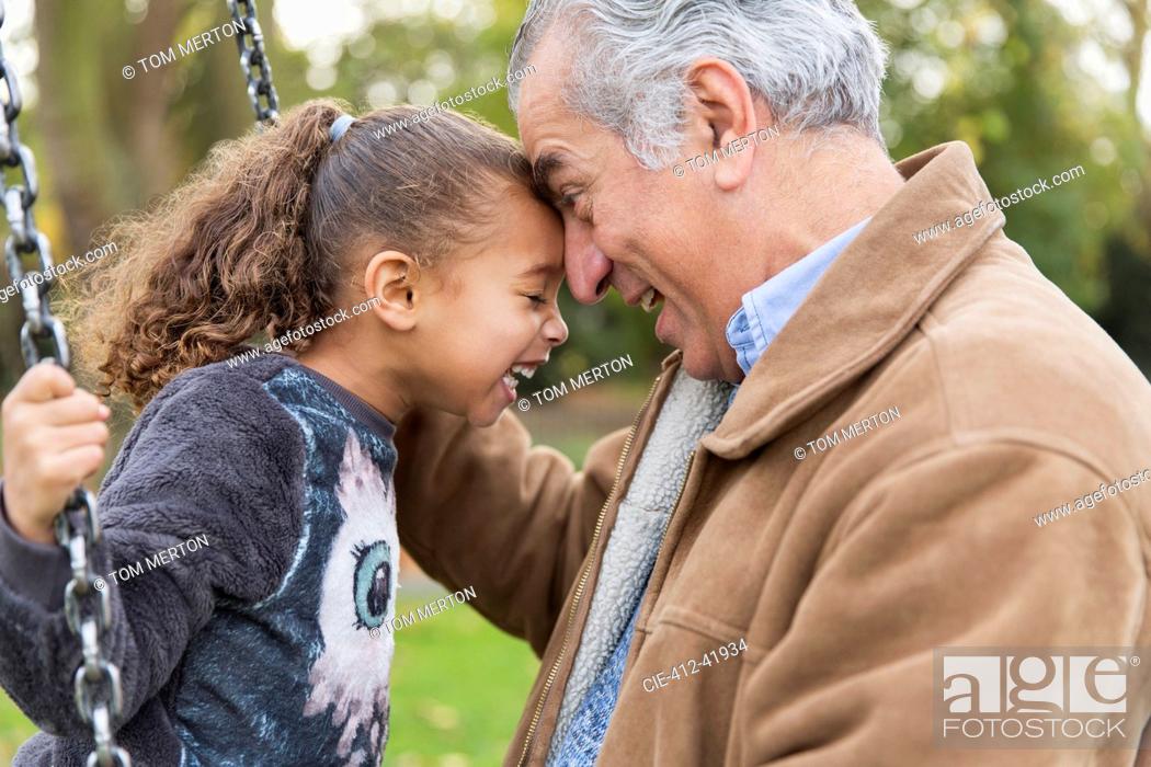 Stock Photo: Playful affectionate grandfather and granddaughter on swing at playground.