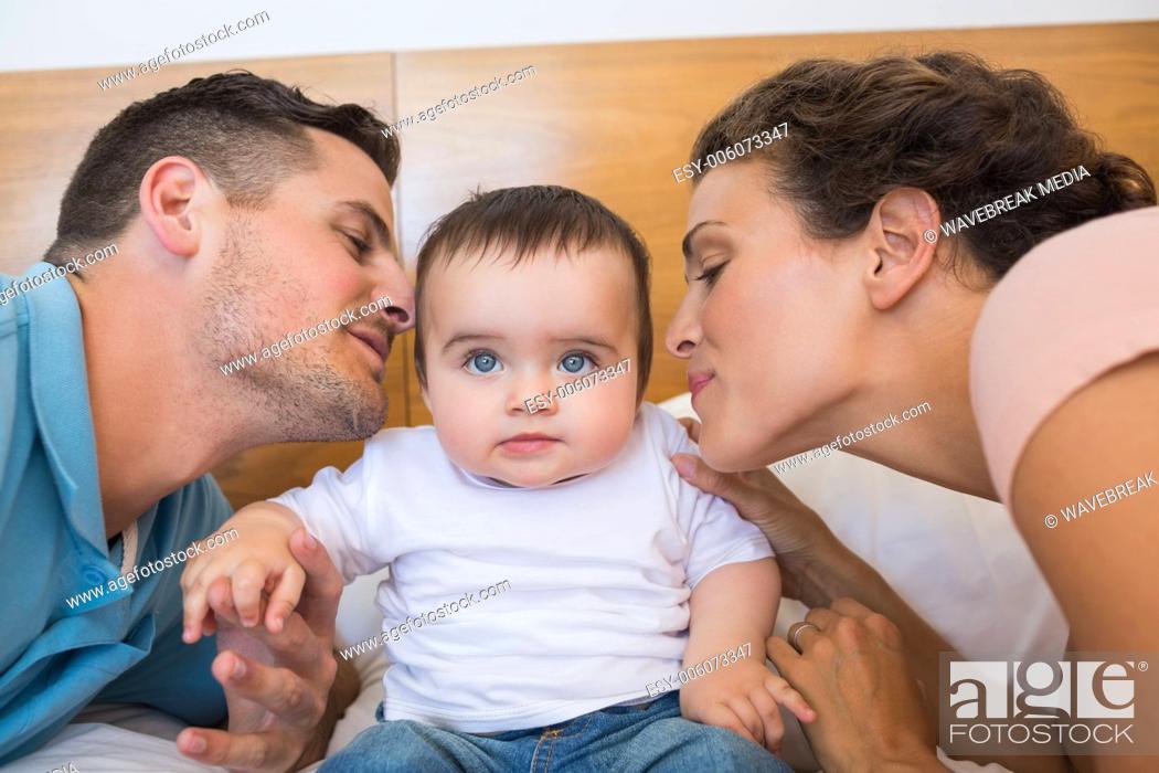 Photo de stock: Parents kissing baby on cheek.
