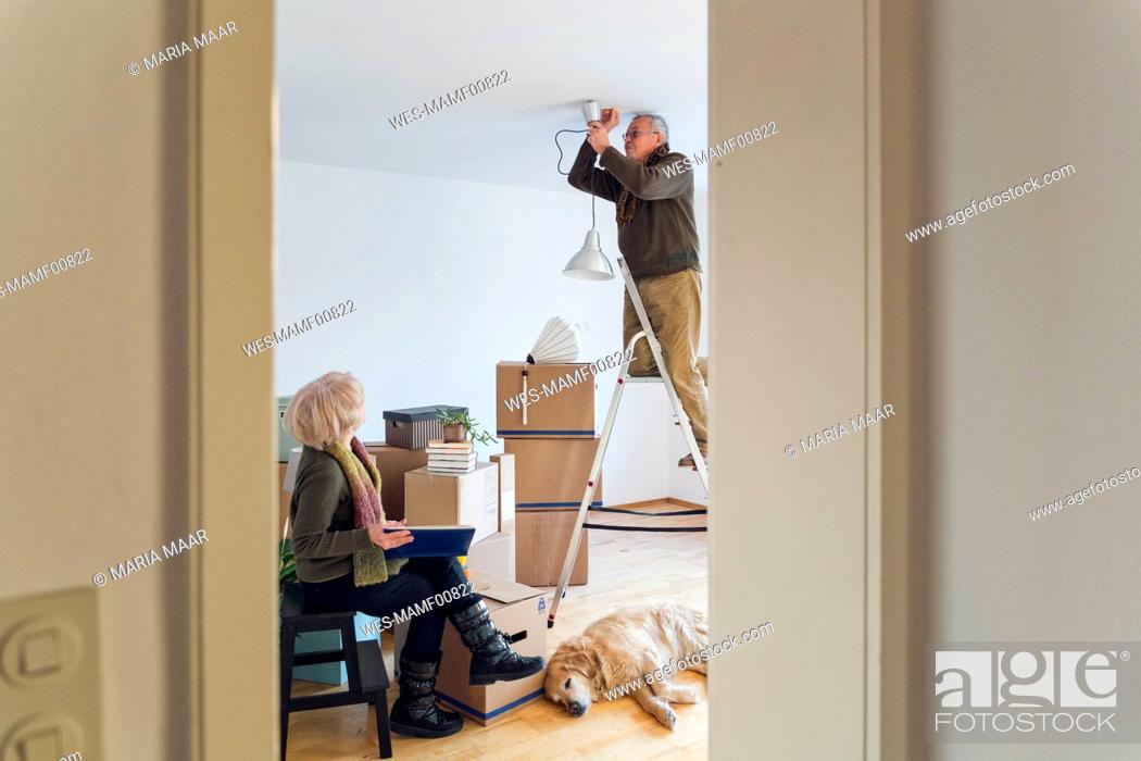 Stock Photo: Senior couple in a new home with man mounting ceiling lamp.