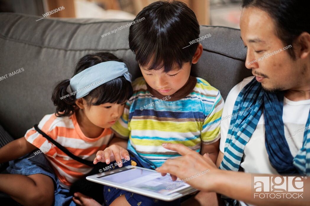 Stock Photo: Man, boy and young girl sitting on a grey sofa, looking at digital tablet.