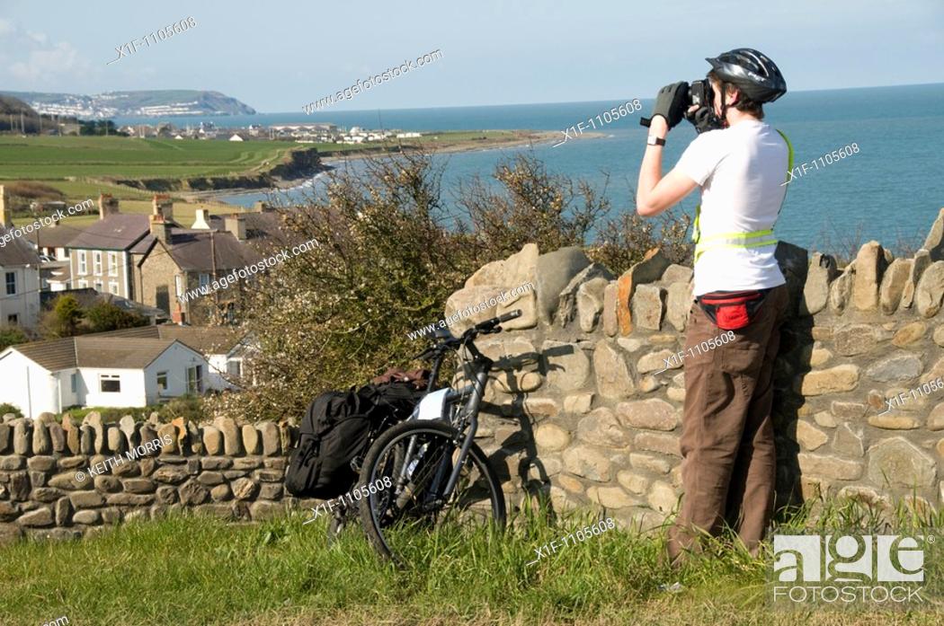 Stock Photo: Young male cyclist taking photograph of Aberarth village on the cardigan bay coast near Aberaeron, ceredigion, west Wales UK.