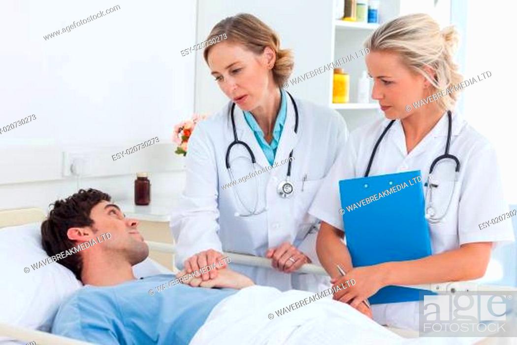 Stock Photo: Two women doctors talking to a patient lying in his bed.