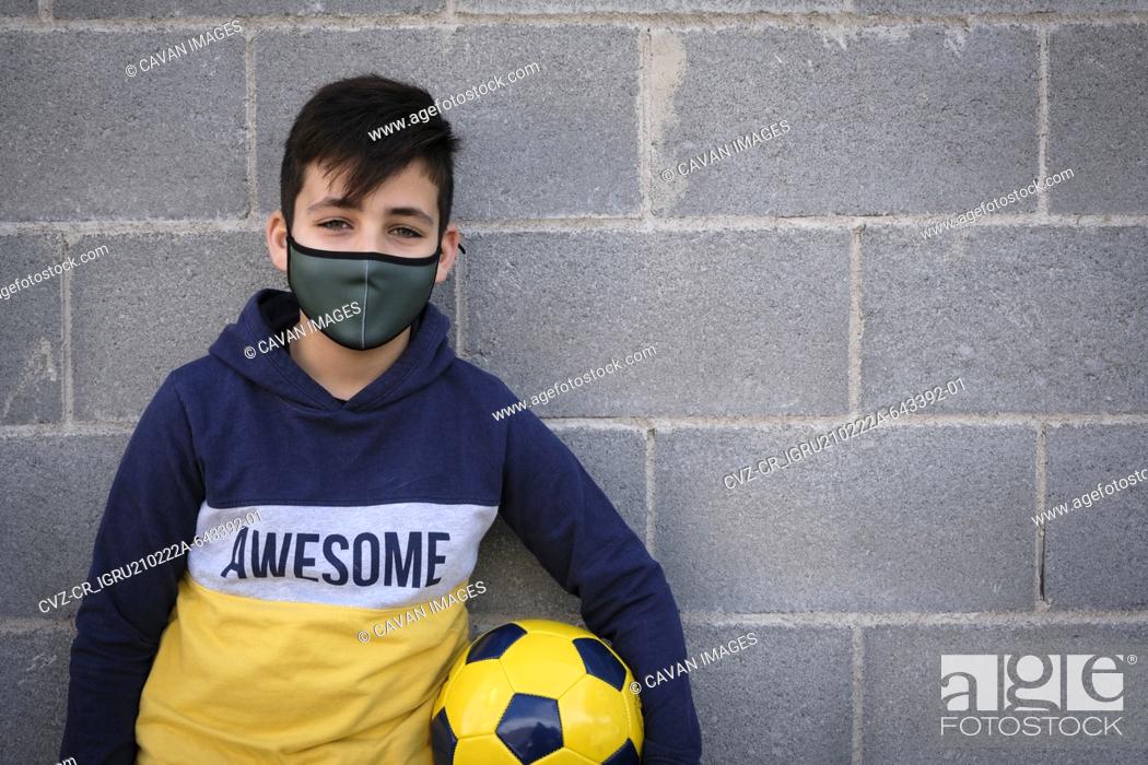 Stock Photo: Kid playing football wearing a green mask. Coronavirus protection.