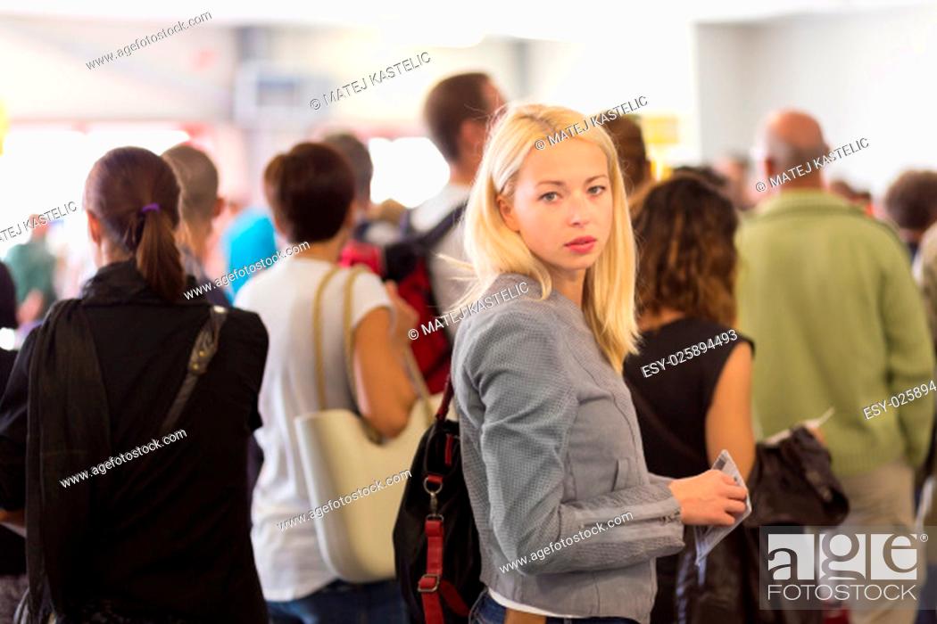 Imagen: Young blond caucsian woman waiting in line with plain ticket in her hands. Lady standing in a long queue to board a plane.