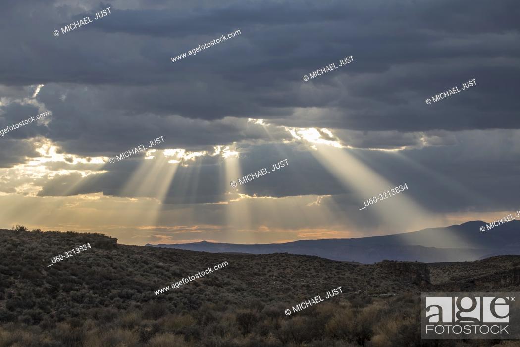 Photo de stock: Stormy skies pass through the Southern Utah landscape and produce sunbeams at sunset.