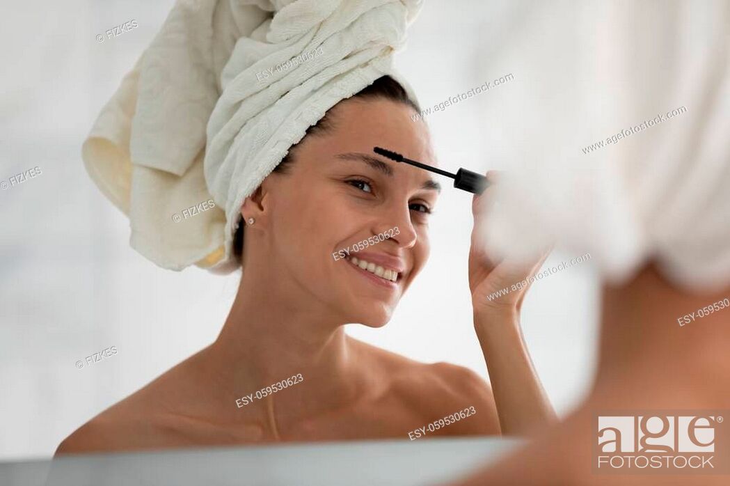 Stock Photo: Head shot close up smiling beautiful woman applying black mascara on eyelashes, attractive woman wearing white bath towel on head putting daily makeup.