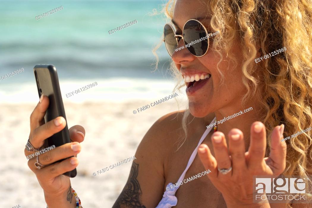 Photo de stock: Happy young pretty adult woman have fun speaking at the phone in summer holiday vacation enjoying beach and sea water. Cheerful side portrait of female people.