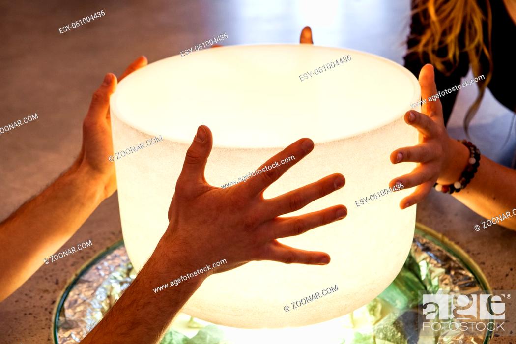 Stock Photo: 4 hands holding a big crystal bowl on top of a light source as part of a recharging meditation ritual.