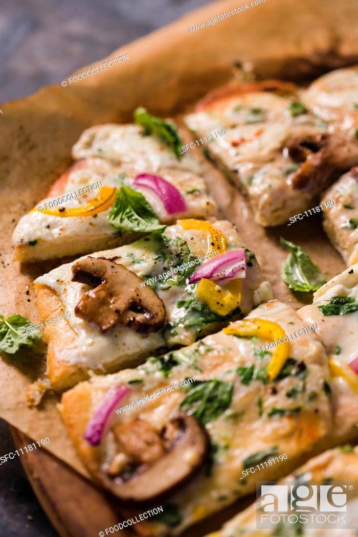 Stock Photo: Veggie Pizza with Mushrooms, Red Onion and Yellow Peppers; Fresh Basil; Sliced on Parchment Paper.