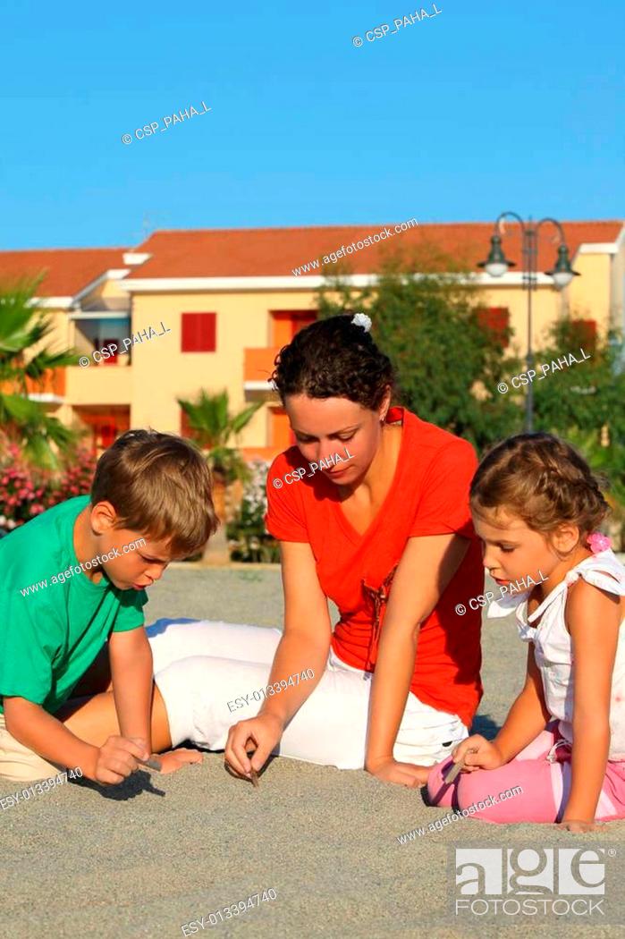 Stock Photo: Woman with two children, girl and boy, draw on sand little sticks in day-time on rest.