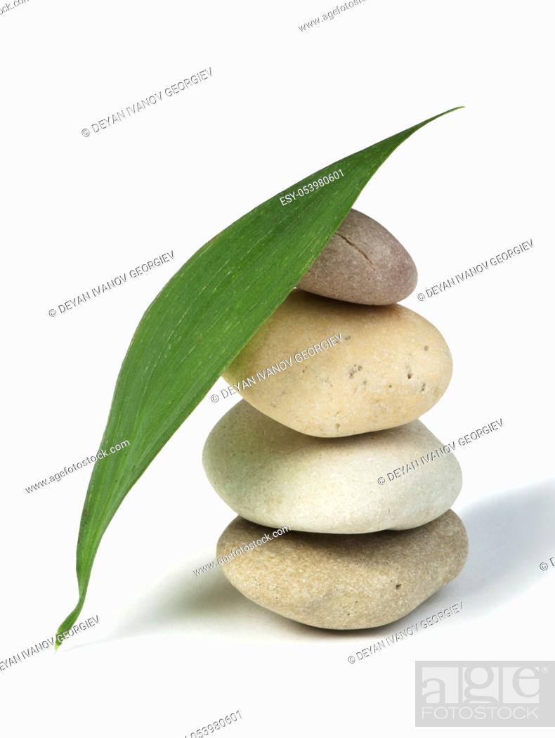 Imagen: Stacked stones and green leafs on white background.