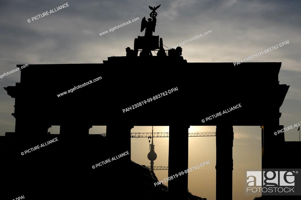 Stock Photo: 19 August 2023, Berlin: The Brandenburg Gate and the TV Tower can be seen in the backlight of the rising sun. People in Berlin and Brandenburg have to prepare.