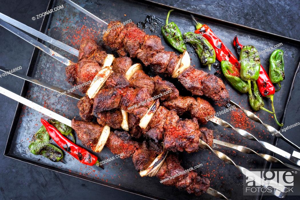 Photo de stock: Traditional Russian lamb shashlik on a barbecue skewer with chili, onion and sumach as top view on a rustic metal tray.
