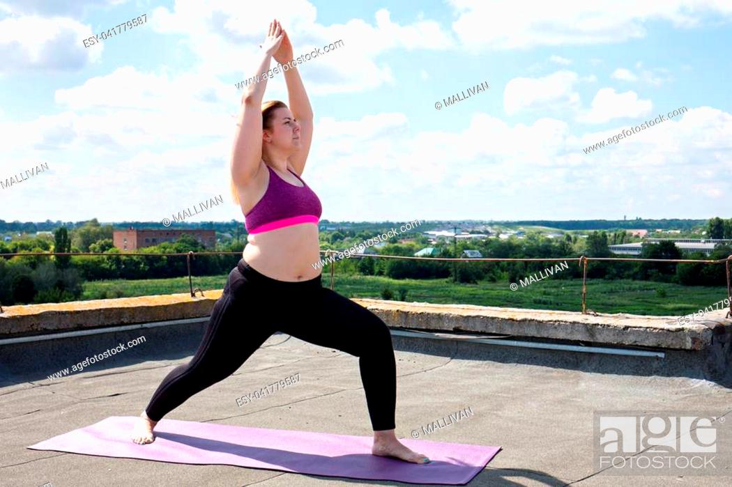 Stock Photo: Young woman doing yoga on the roof of a building.