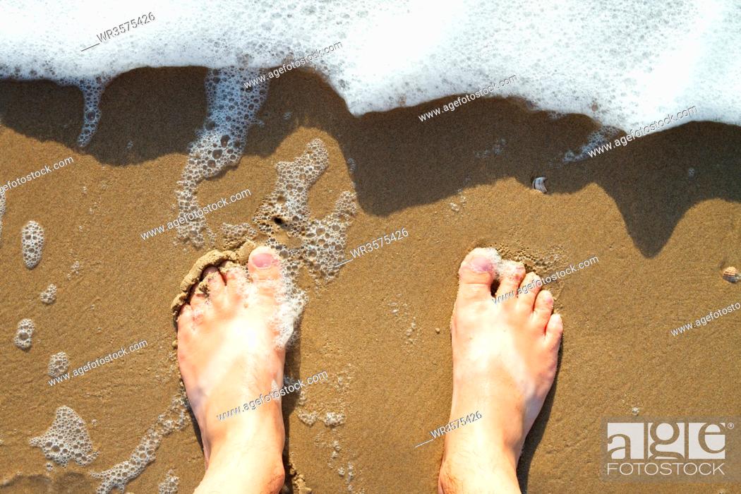 Stock Photo: Male feet standing on the beach watching the water waves from above.