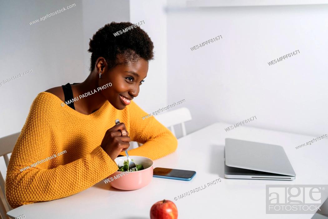 Stock Photo: Happy young woman having healthy breakfast at table while looking away.