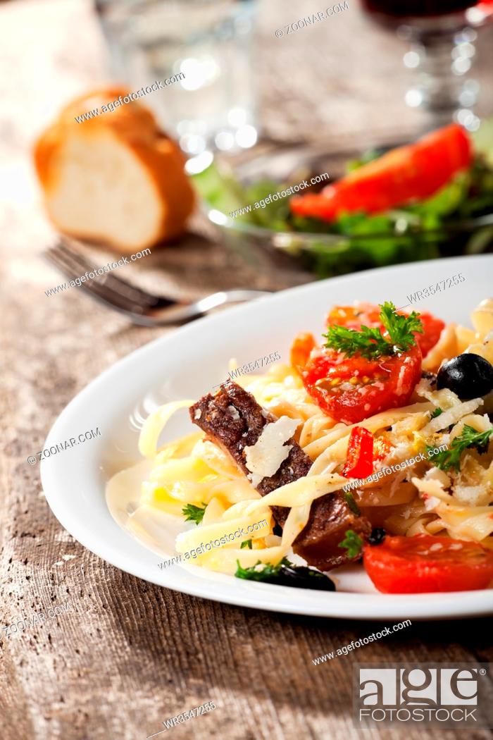 Imagen: frische Pasta mit Tomaten und Oliven auf einem Teller.