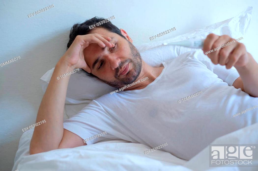 Stock Photo: Sick man in bed measuring temperature feeling fever.