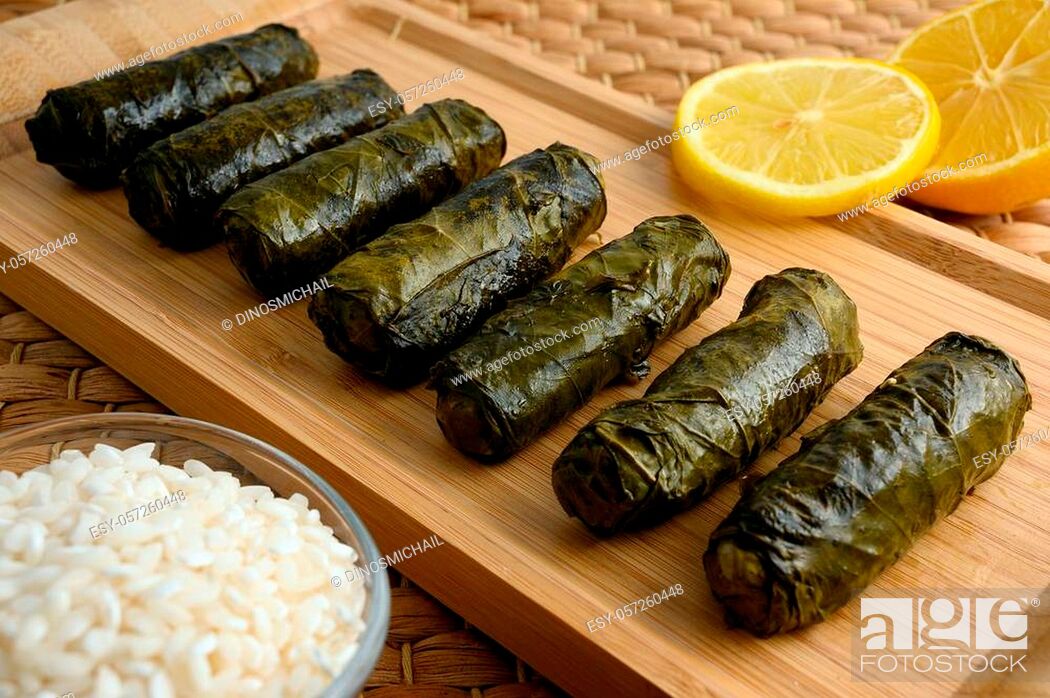 Stock Photo: Delicious stuffed grape leaves (the traditional dolma of the mediterranean cuisine) on wooden tray board with lemon and small glass bowl of raw rice.
