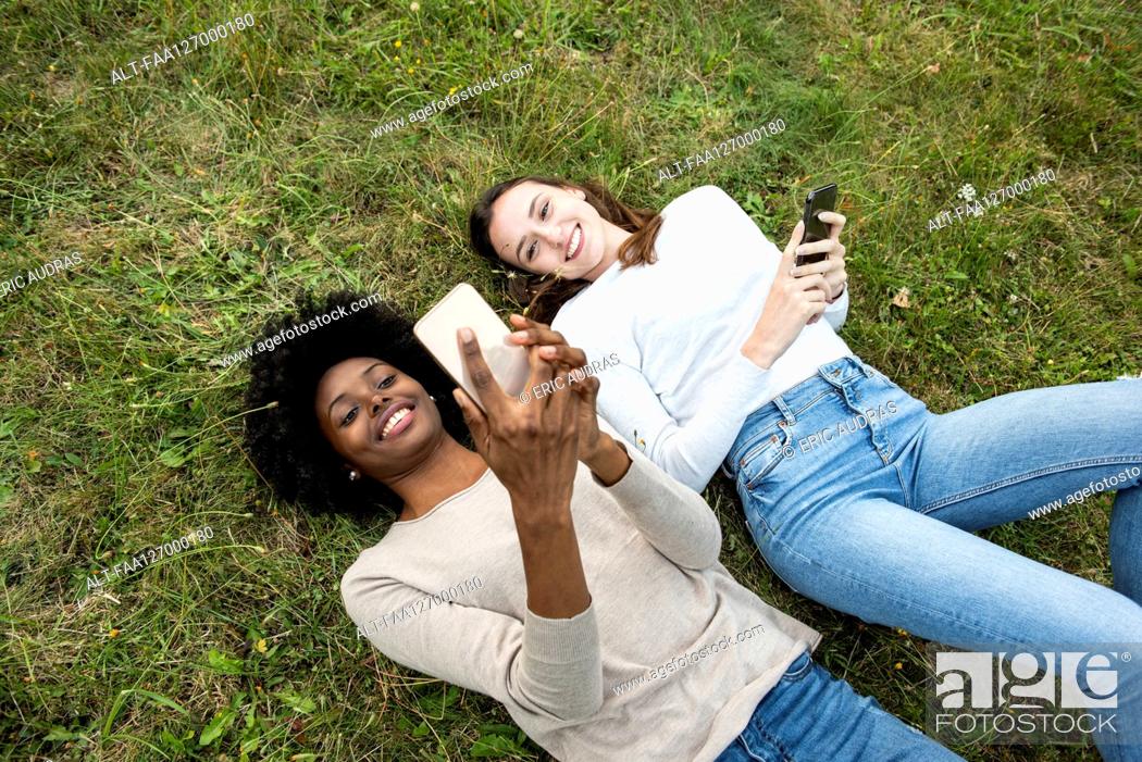 Photo de stock: Young female friends lying on grass while using smart phone in park.