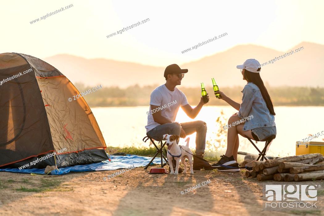 Stock Photo: Young adult Asian couple drinking beer beside their tent campsite while sunset. Camping trip with dog outdoor activity campsite concept.
