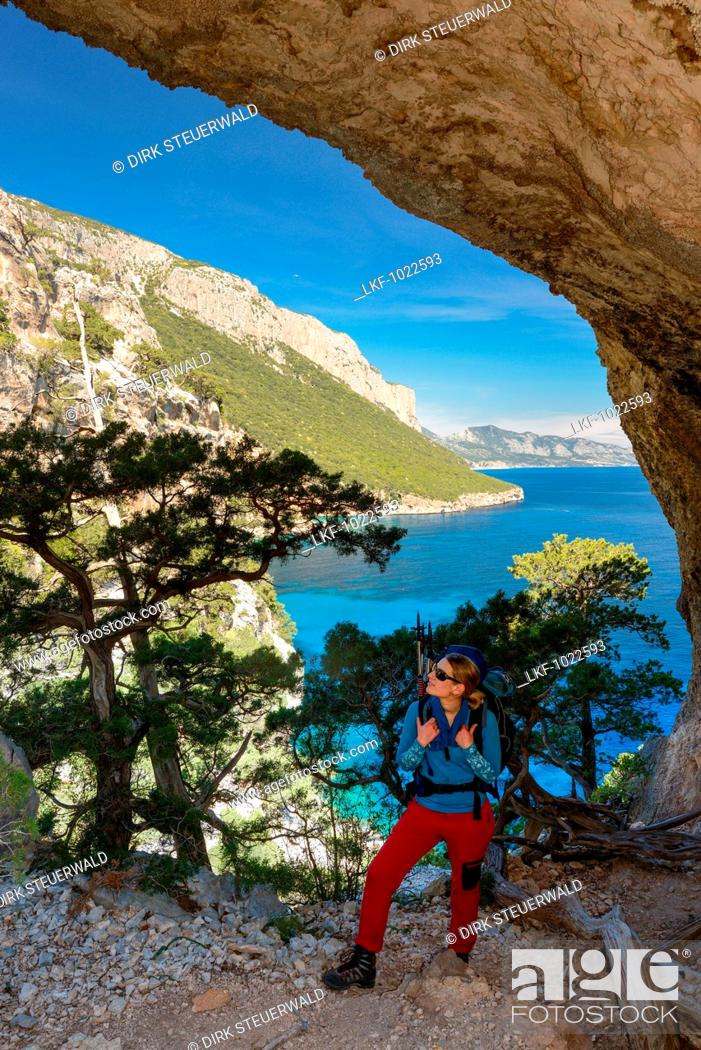 Stock Photo: A young woman with trekking gear hikes through the rock arch Arcu su Feilau at the mountainous coast above the sea, Golfo di Orosei, Selvaggio Blu, Sardinia.
