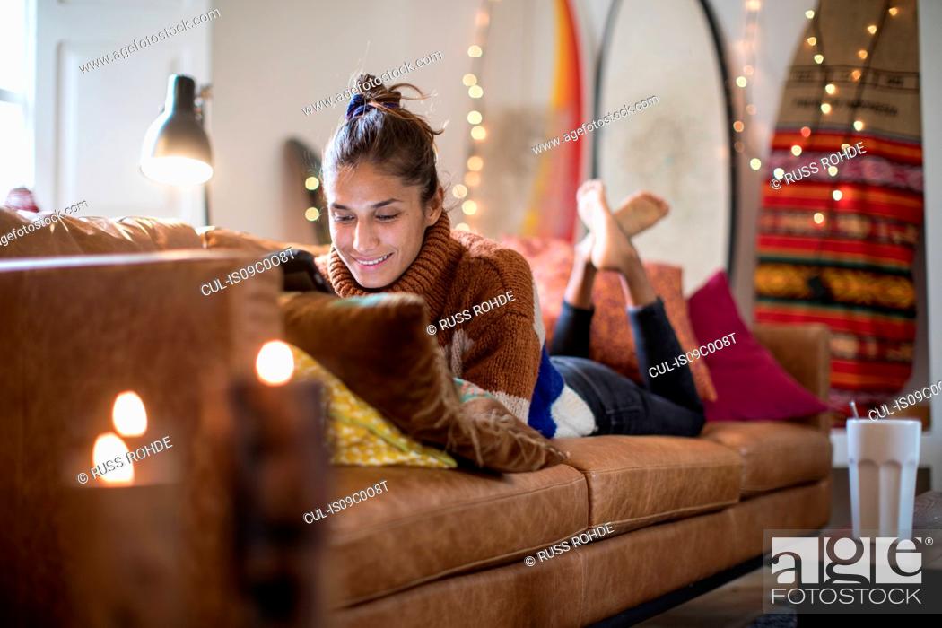 Stock Photo: Young woman lying on living room sofa looking at laptop.