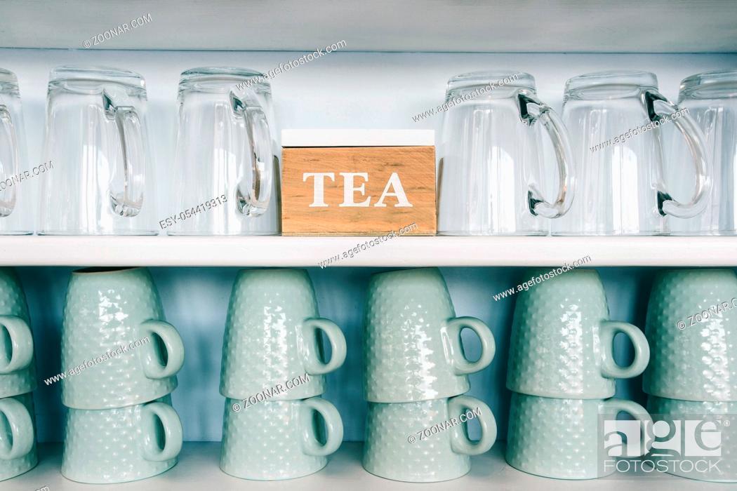 Imagen: tea cups and coffee mugs on a kitchen shelf with a tea box Rack focus. Close up. wooden shelf.
