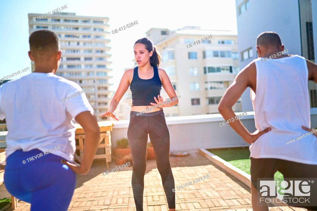 Stock Photo: Young female yoga instructor teaching class on sunny urban rooftop.