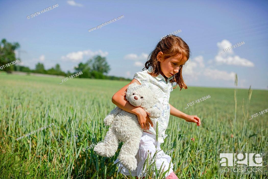 Imagen: Girl with teddy bear walking in sunny, rural green field.