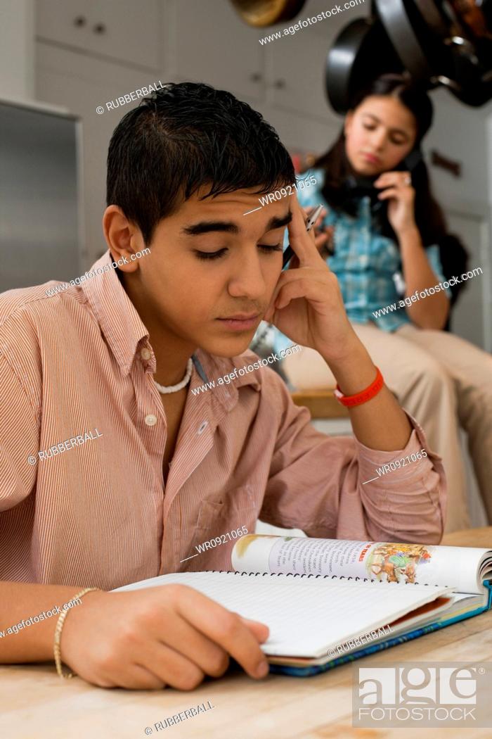 Stock Photo: Boy doing homework with girl talking on phone.
