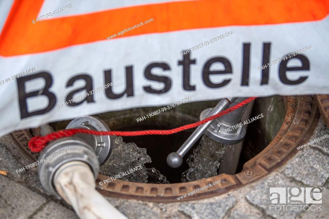 Stock Photo: 06 August 2019, Bavaria, Munich: Water pumped out of the S-Bahn tunnels flows into a gully cover blocked off by THW. Photo: Lino Mirgeler/dpa.