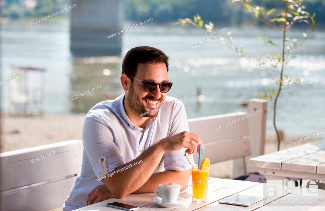 Stock Photo: Handsome man with sunglasses drinking coffee and juice in cafe on beach. Enjoying morning beside river.