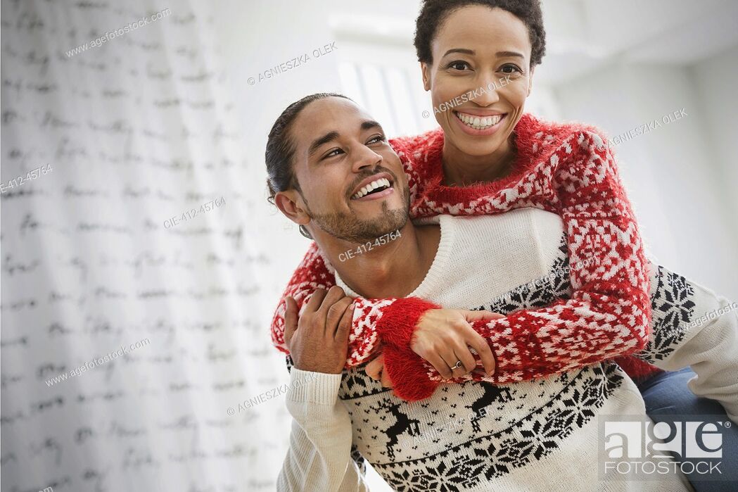 Imagen: Portrait happy, playful couple in Christmas sweaters piggybacking.