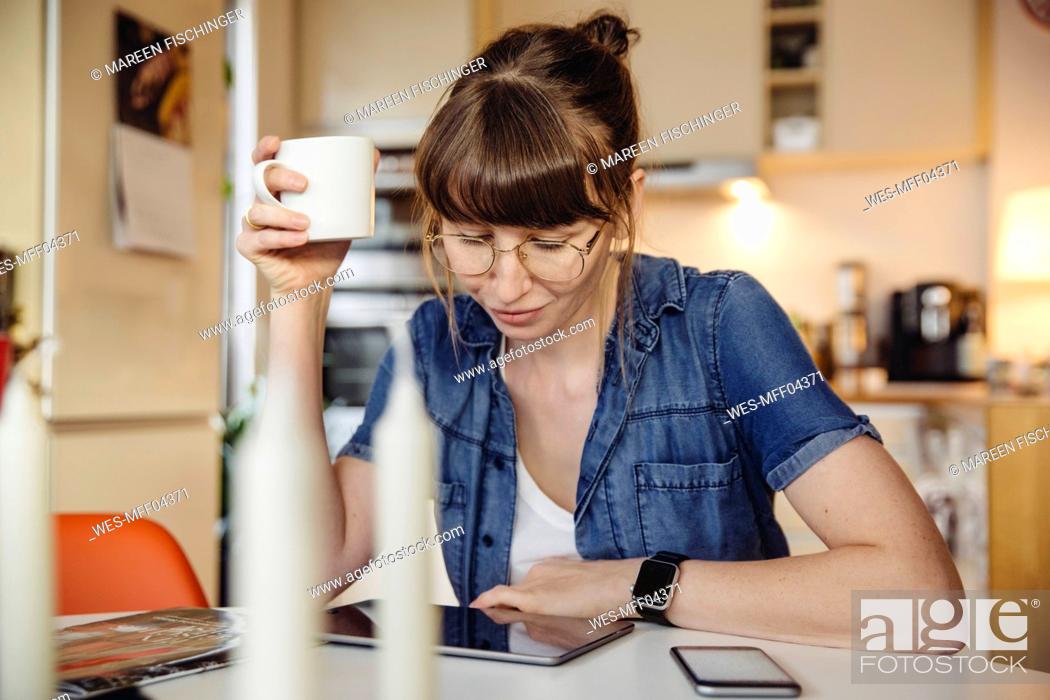 Stock Photo: Woman sitting with cup of coffee at table in the kitchen using tablet.