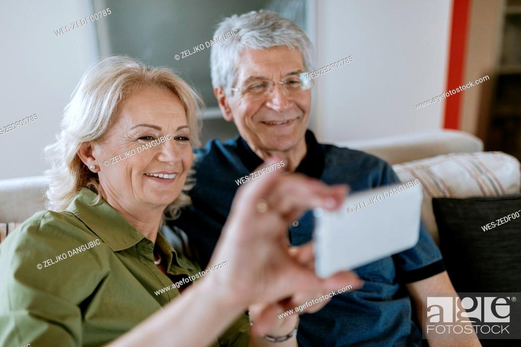 Imagen: Senior couple at home sitting on couch taking a selfie.