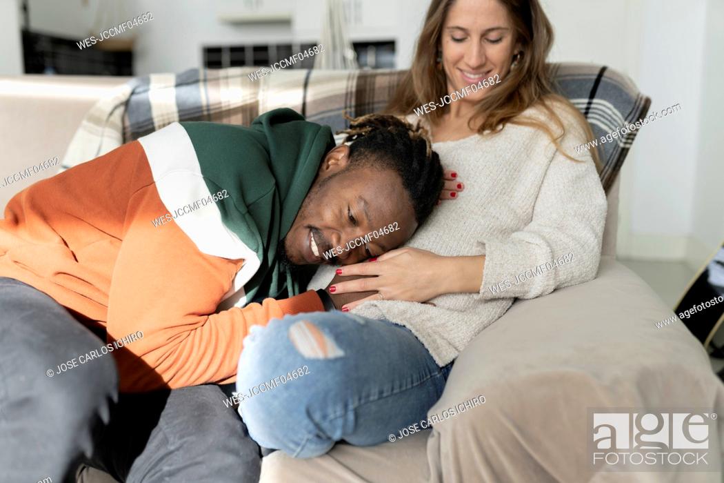 Photo de stock: Happy man putting head on pregnant woman's belly sitting at home.