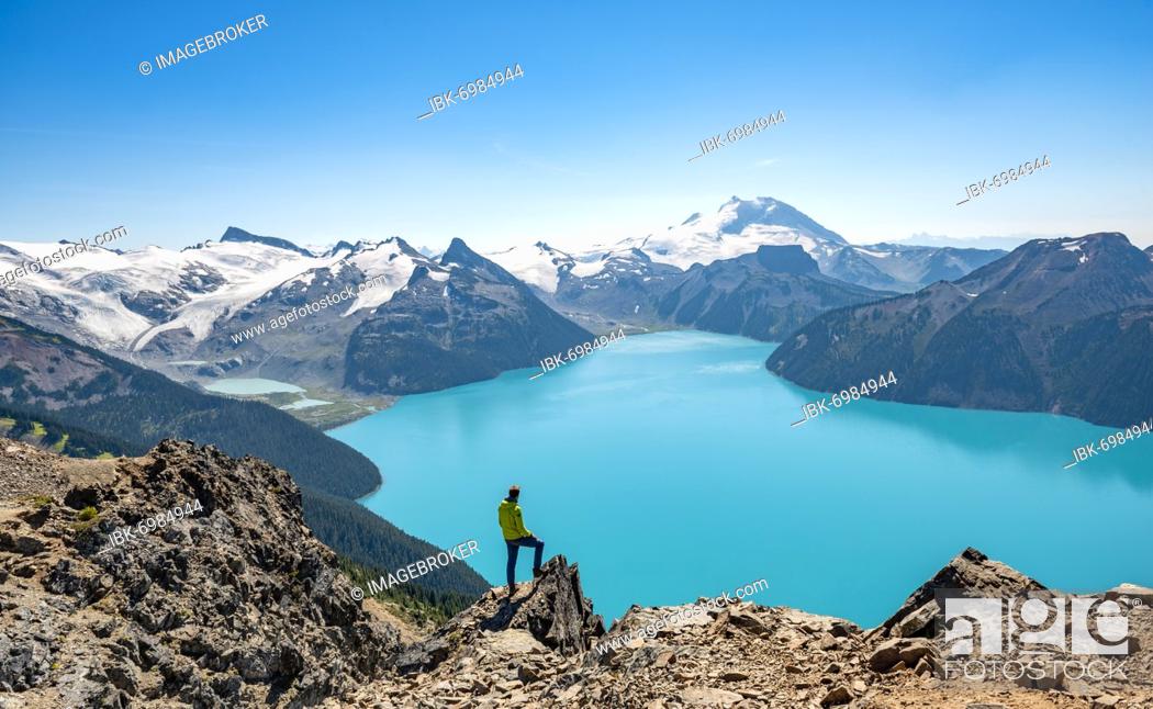 Stock Photo: Young man standing on a rock, looking into the distance, view of mountains and glacier with turquoise blue lake Garibaldi Lake, peaks Panorama Ridge.