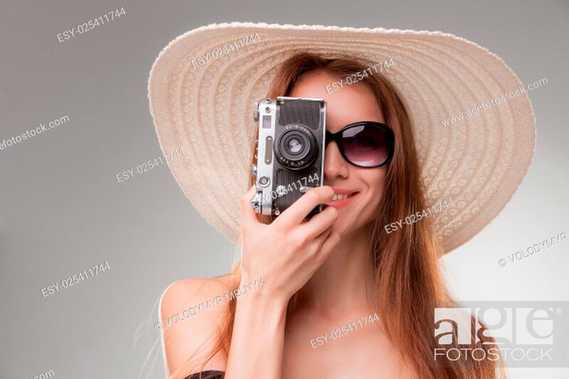 Stock Photo: Girl in broad-brimmed hat and sunglasses with retro camera isolated on gray background.