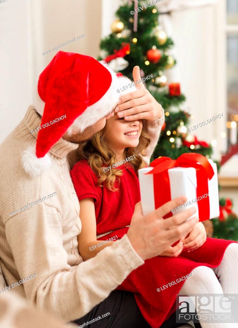 Stock Photo: family, christmas, x-mas, winter, happiness and people concept - smiling father surprise daughter with gift box covering eyes with hand.