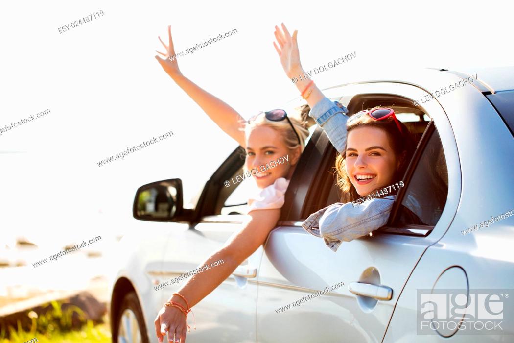 Photo de stock: summer vacation, holidays, travel, road trip and people concept - happy teenage girls or young women in car at seaside waving hands.