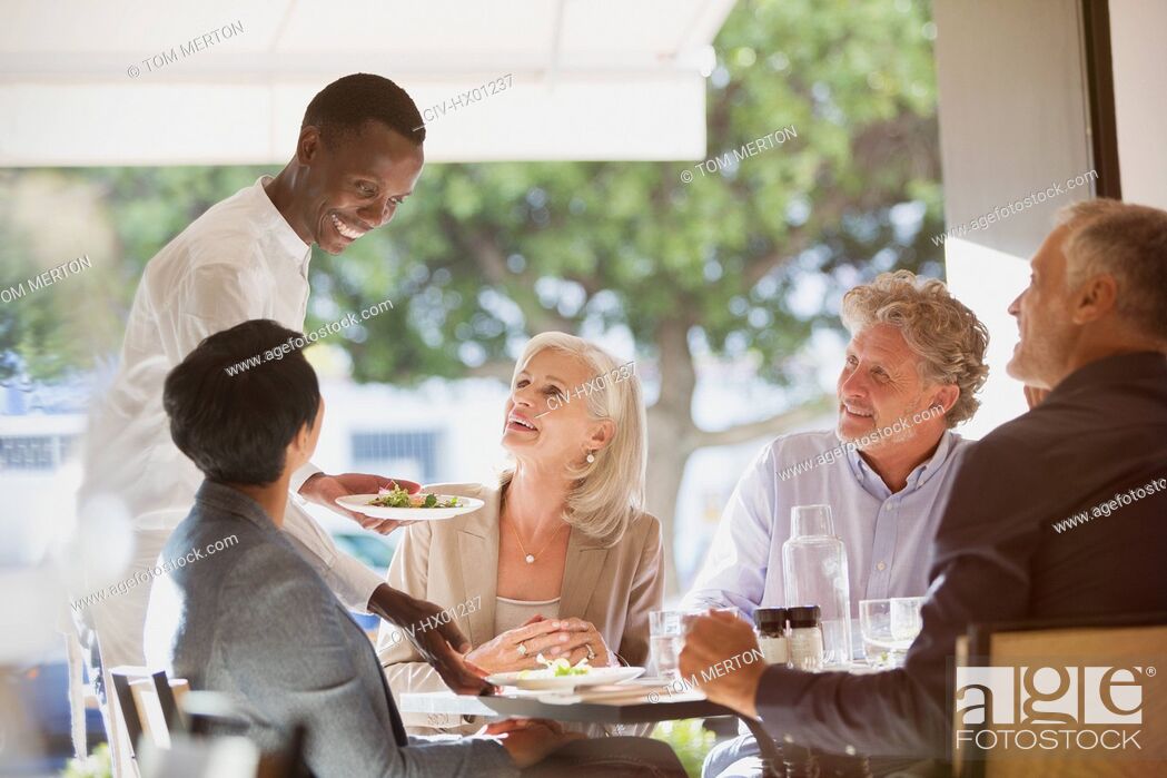 Stock Photo: Waiter serving food to couples at restaurant table.