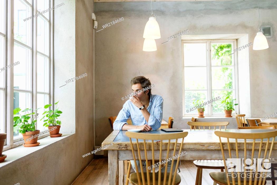 Stock Photo: Man drinking coffee while looking through window at restaurant.