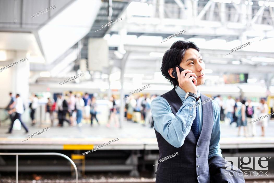 Stock Photo: Businessman wearing suit standing on train station platform, holding mobile phone.