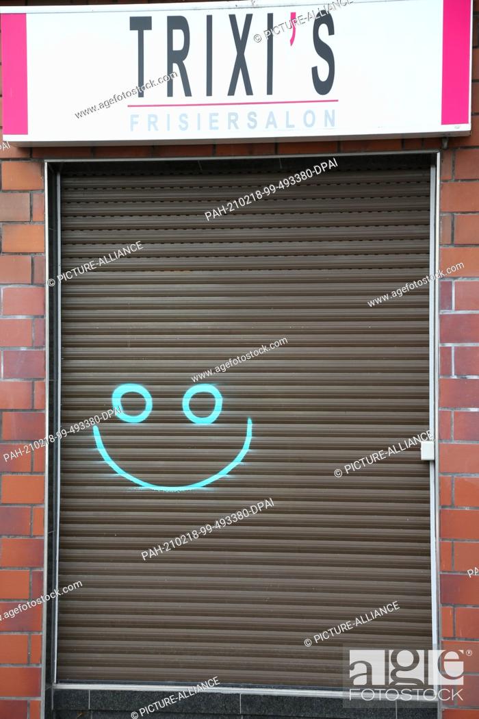Stock Photo: 18 February 2021, North Rhine-Westphalia, Bielefeld: The window of a hairdressing salon is closed with a blind, a smiling face is painted on it.